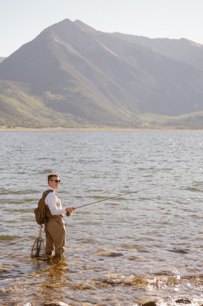 Groom fly fishing with mountains in the background