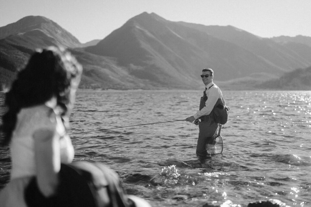 Groom fly fishing with bride at his adventure elopement