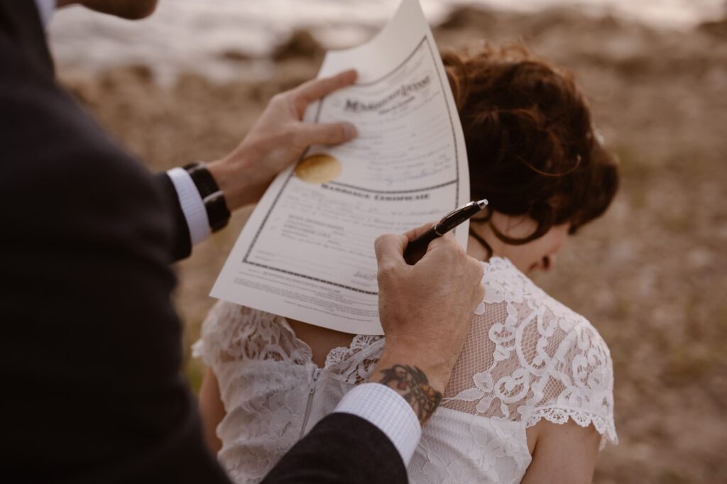 Groom signing marriage license on bride's back