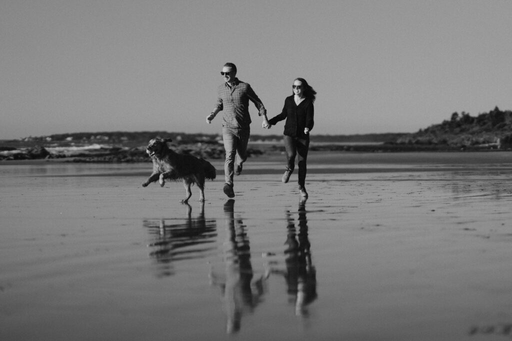 Black and white photo of couple running and playing with their golden retriever