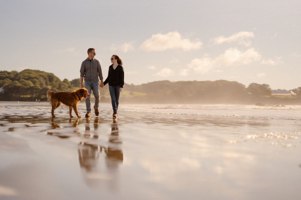Couple walking along the ocean with their dog