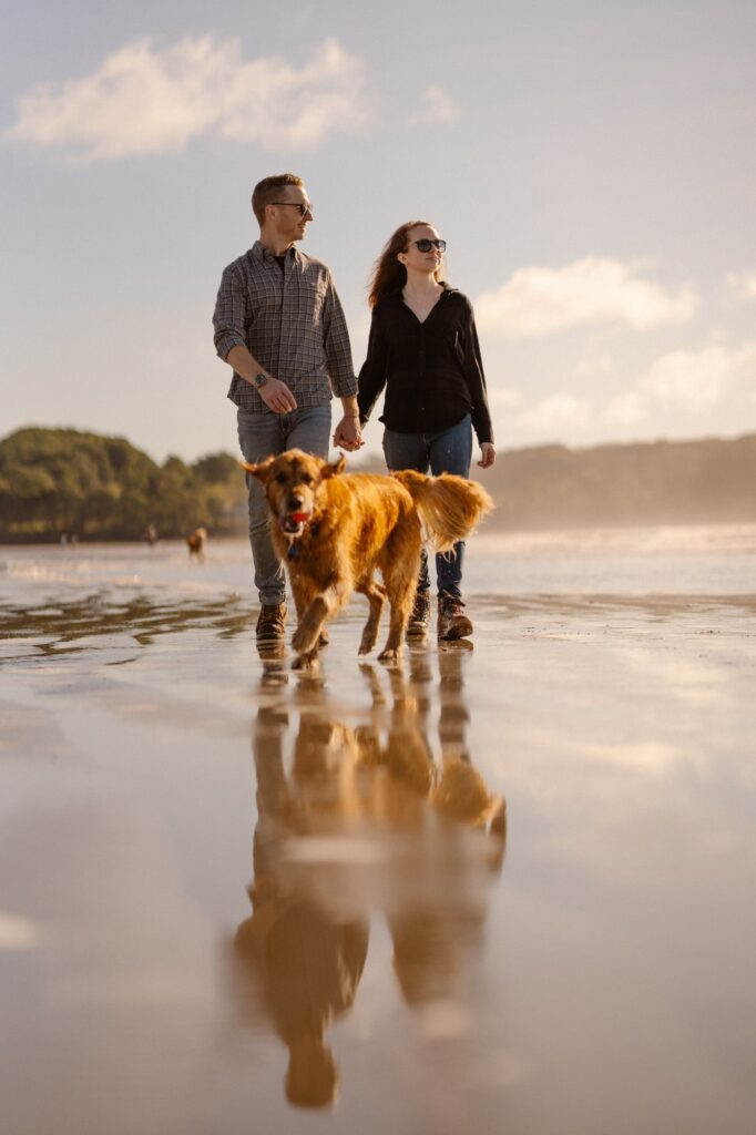 Dog running while couple walks down the beach during lifestyle portrait session