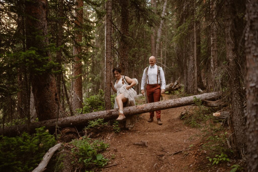 Bride stepping over a large tree on the hiking trail in her wedding dress and hiking boots