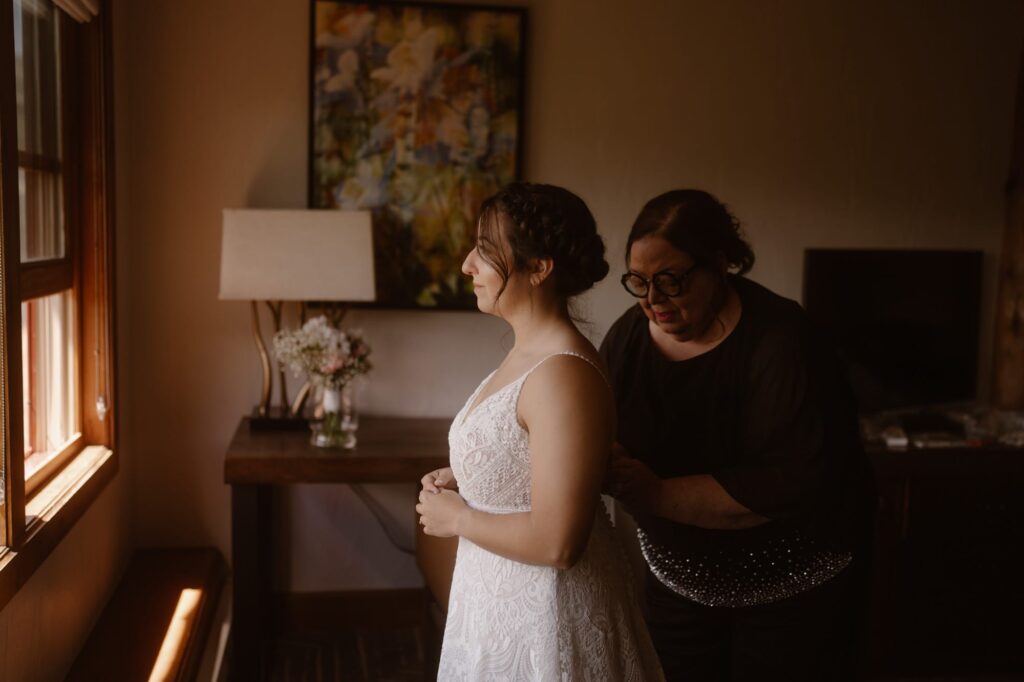 Bride and her mother putting on the wedding dress