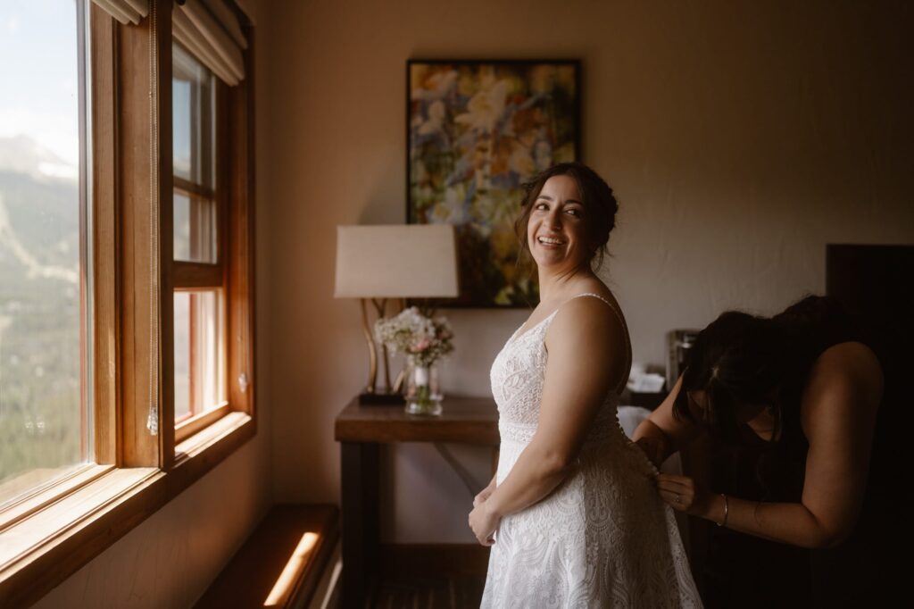 Bride looking over her shoulder laughing as the wedding dress gets fastened