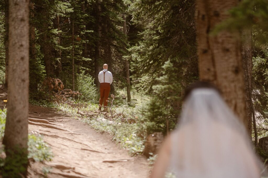 Bride walking up to the groom in the forest for the first look on their elopement day in Colorado