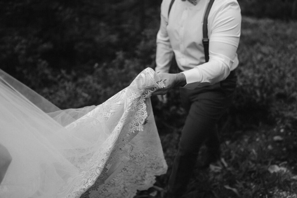 Black and white detail shot of groom holding bride's dress