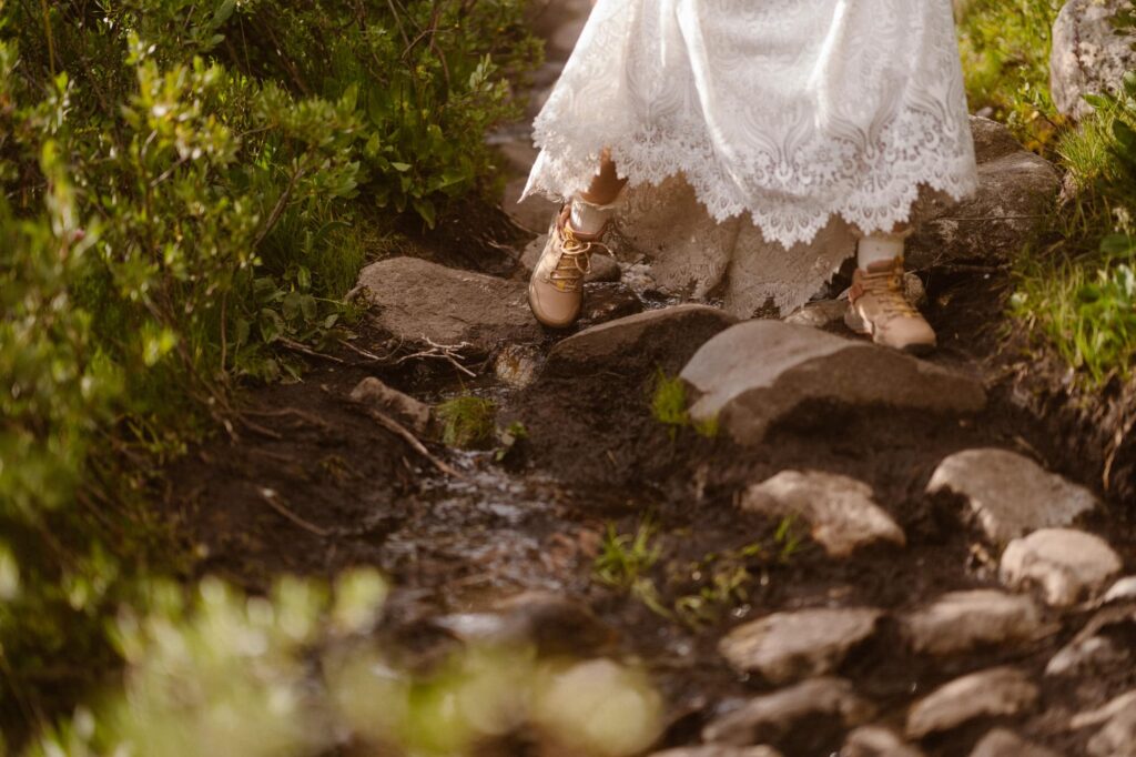 Bride with hiking boots stepping on rocks to avoid muddy trail