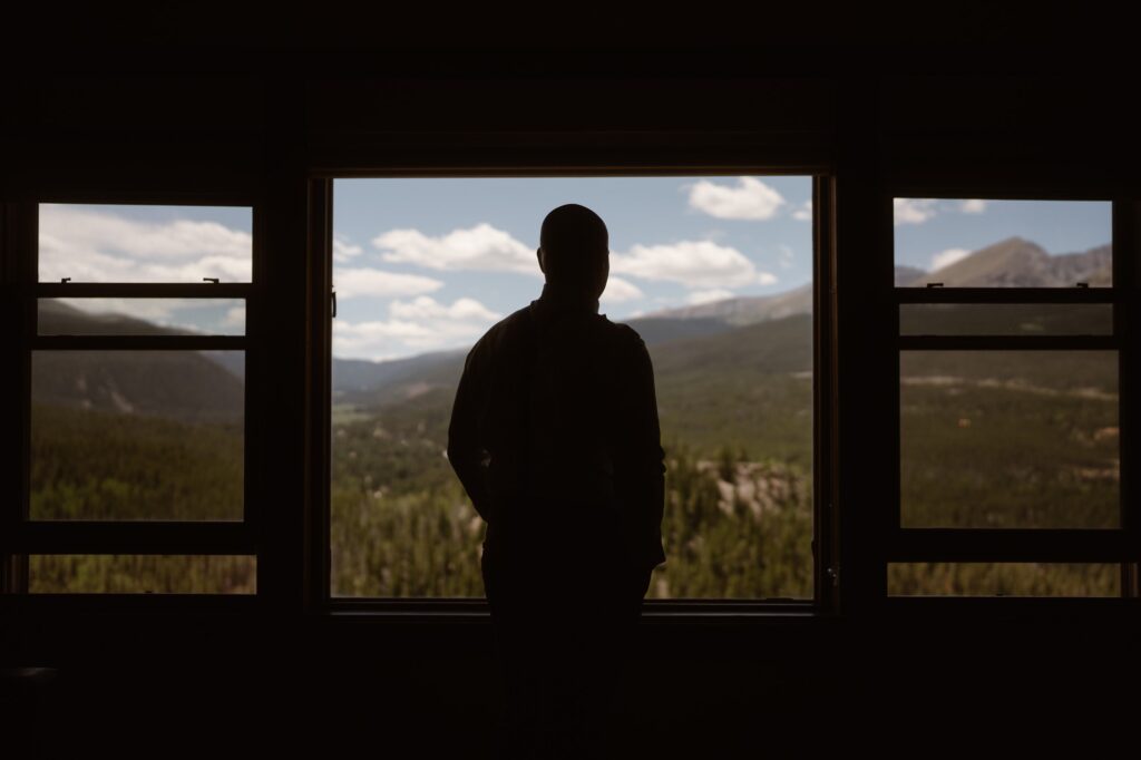 Groom looking out window into the mountains
