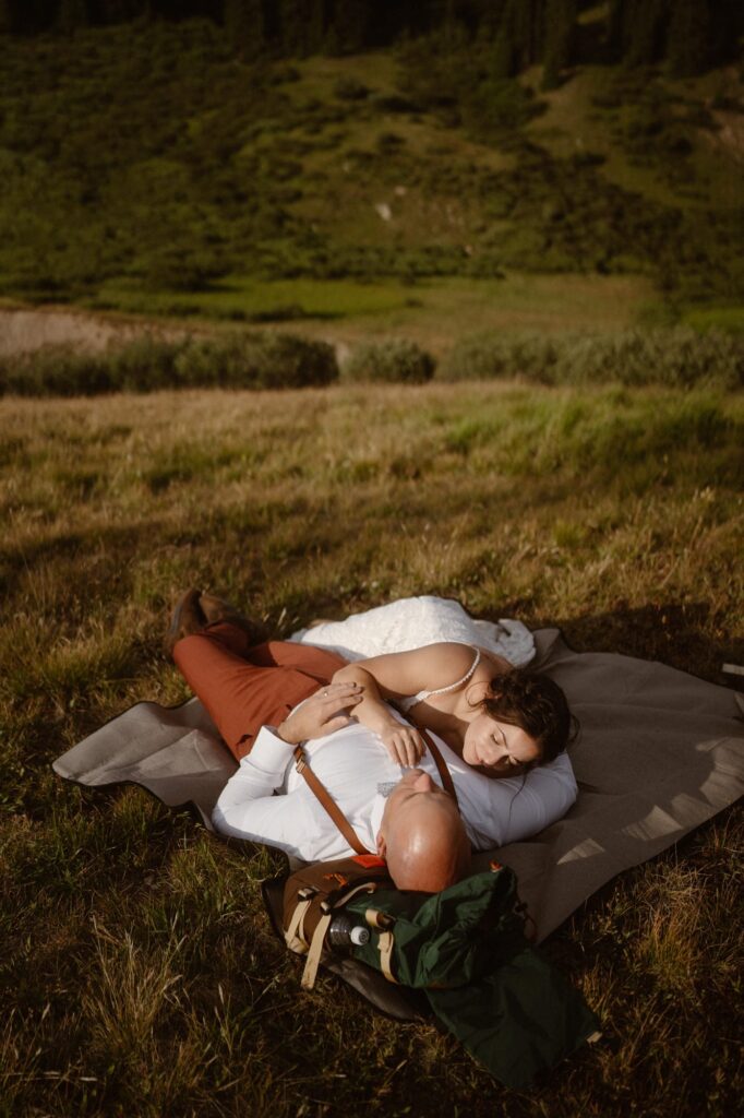 Couple snuggled together, laying down on a blanket at their elopement