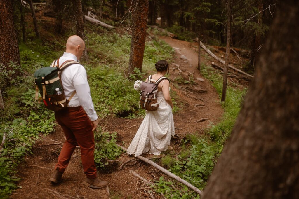 Bride and groom hiking with backpacks on through the forest