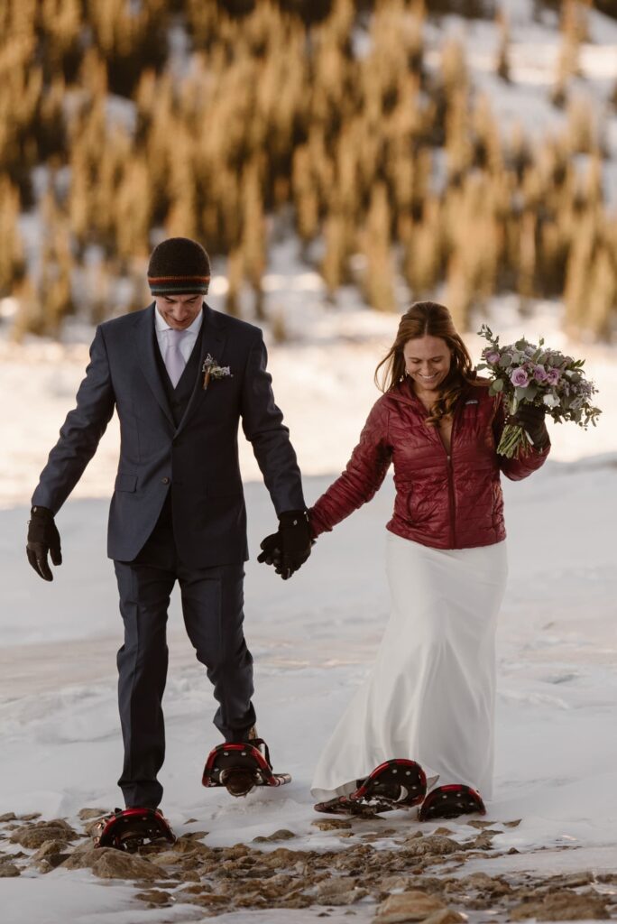 Couple walking through snow in their wedding attire with snowshoes