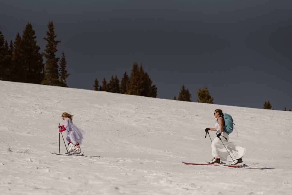 Bride and daughter skiing up a hill in wedding attire