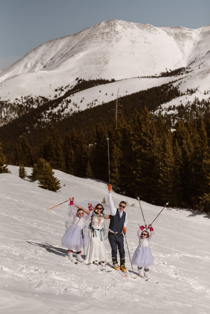 Family poses with skis and ski poles with mountains in the distance on their wedding day