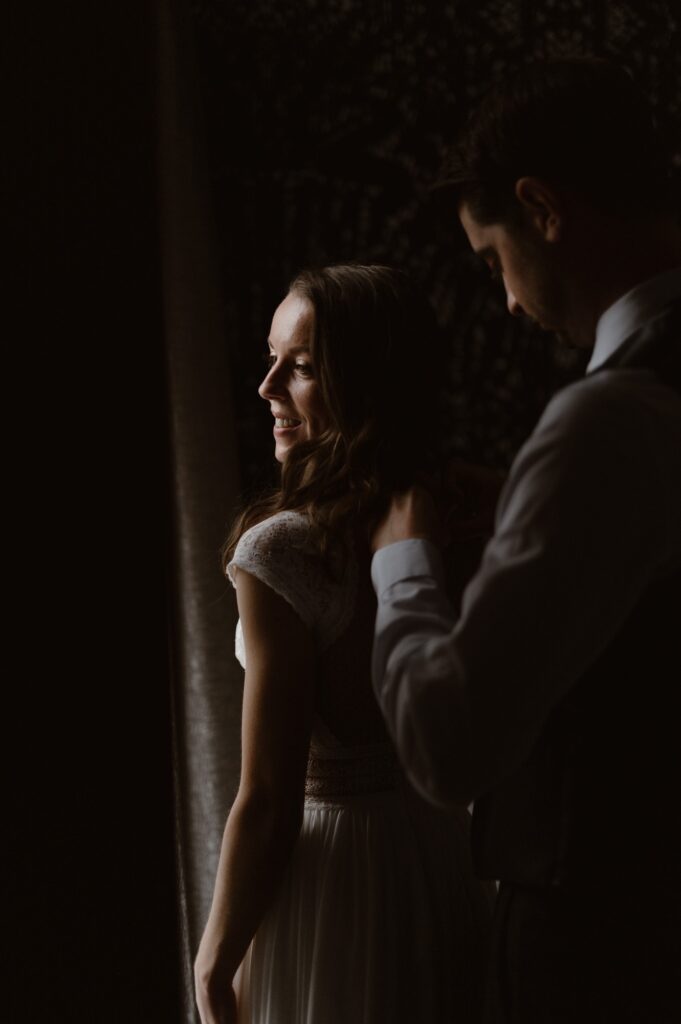 Bride looking over her shoulder as groom fastens her wedding dress