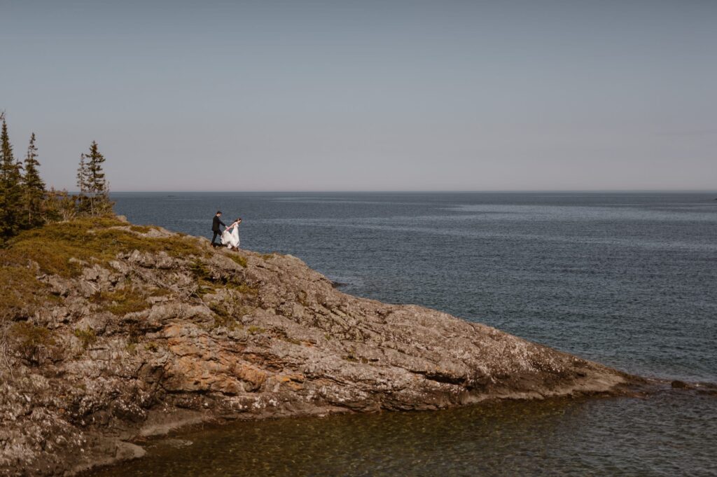 Wide view of bride and groom hiking along rocky shoreline on Lake Michigan
