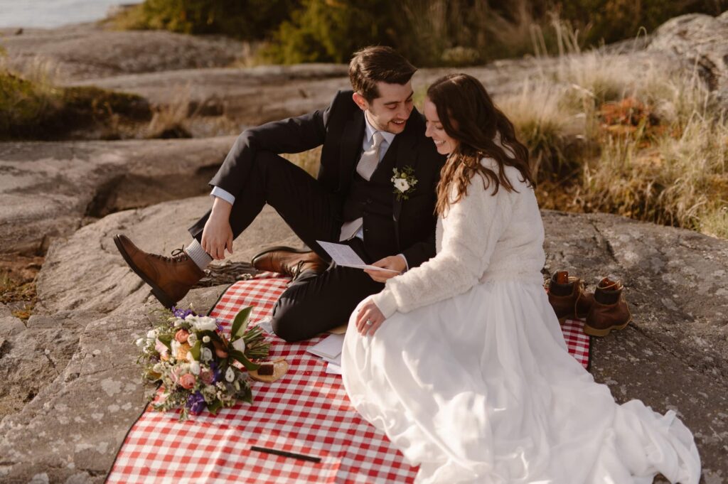 Bride and groom reading letters from loved ones on a red and white plaid picnic blanket