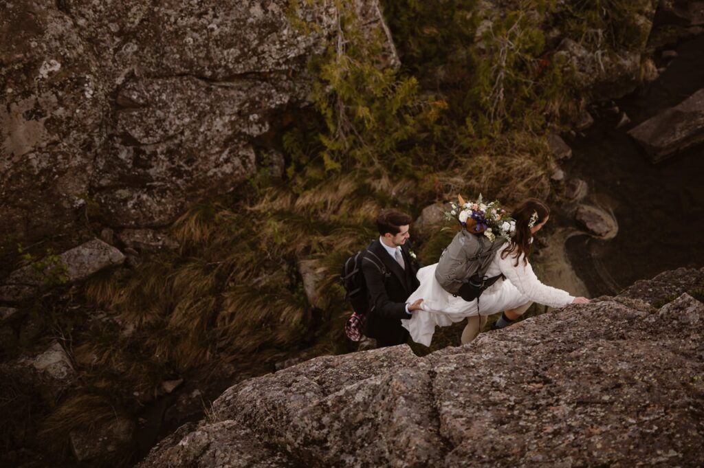 Couple climbing up a boulder on their elopement day