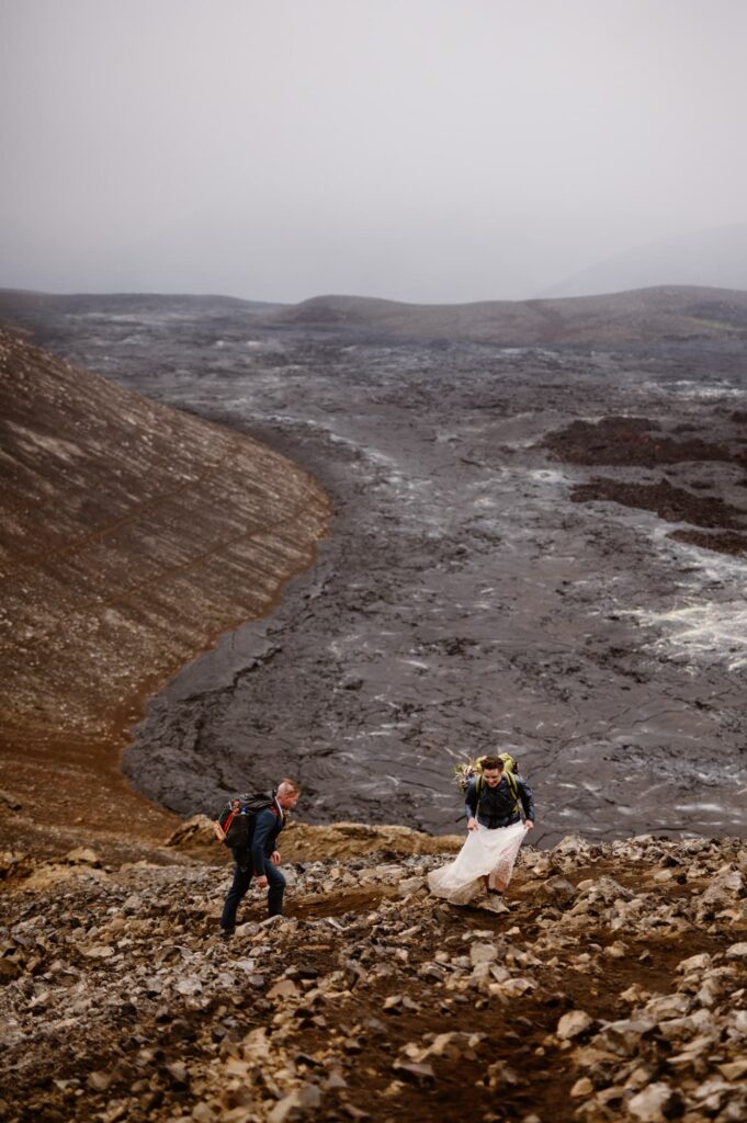 Bride and groom hiking up a mountain overlooking a lava field in Iceland