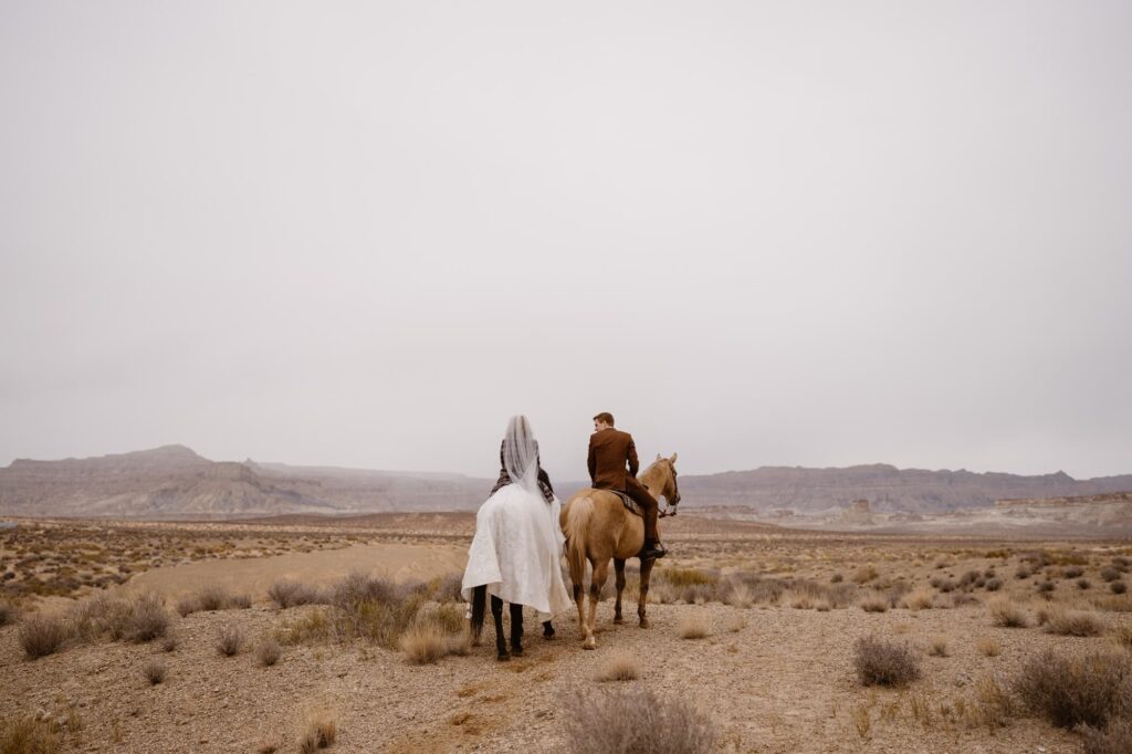 Bride and groom riding horseback through the desert