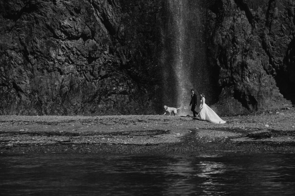 Bride and groom walking in front of a waterfall in Alaska