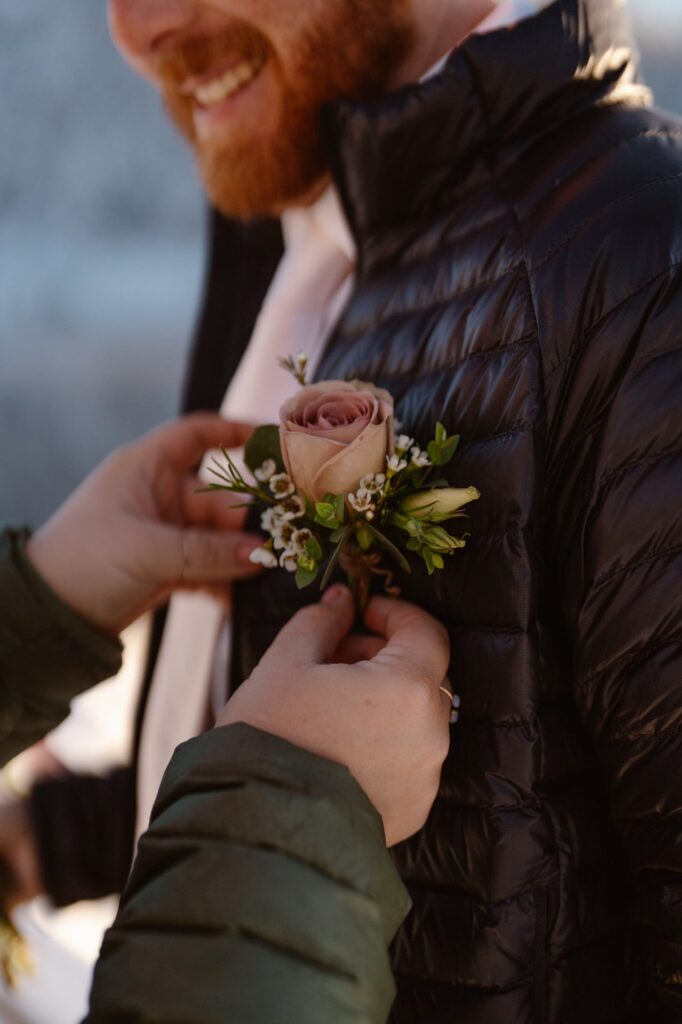 Bride putting the boutonniere on her groom's puffy jacket