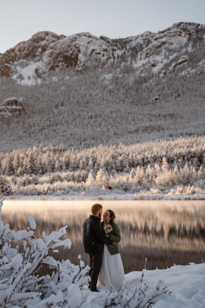 Bride and groom taking wedding portraits at a snowy mountain lake
