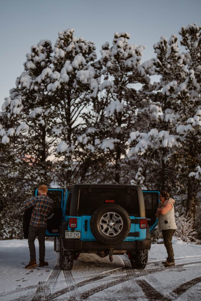 Couple getting out of their blue Jeep in the snow before their wedding