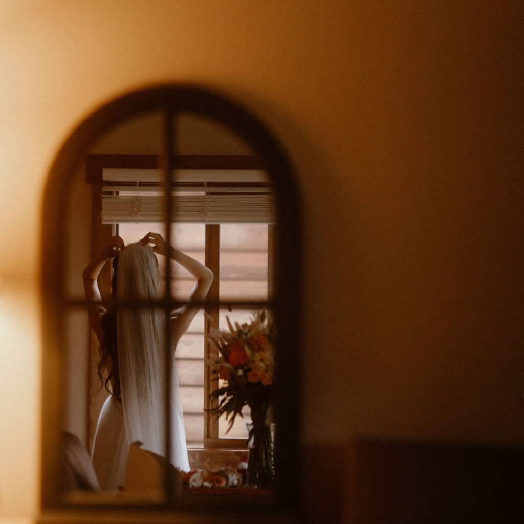Bride putting on her veil as she looks out the window