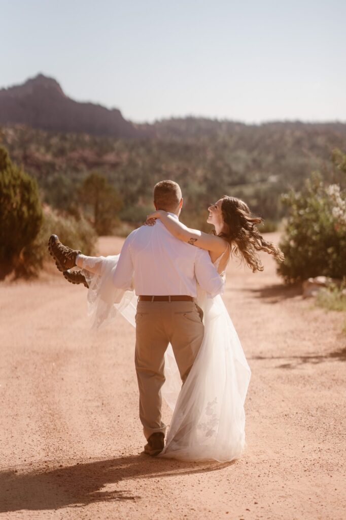 Groom carrying his bride down a dirt road
