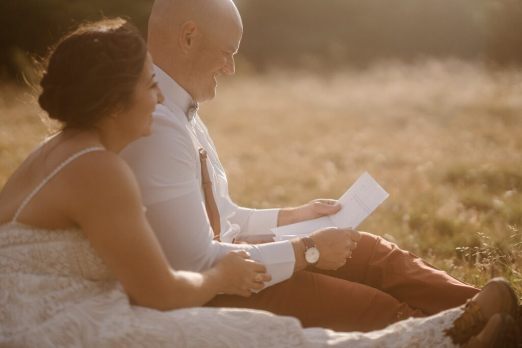 Couple sitting in a meadow and reading letters from family and friends during their micro wedding