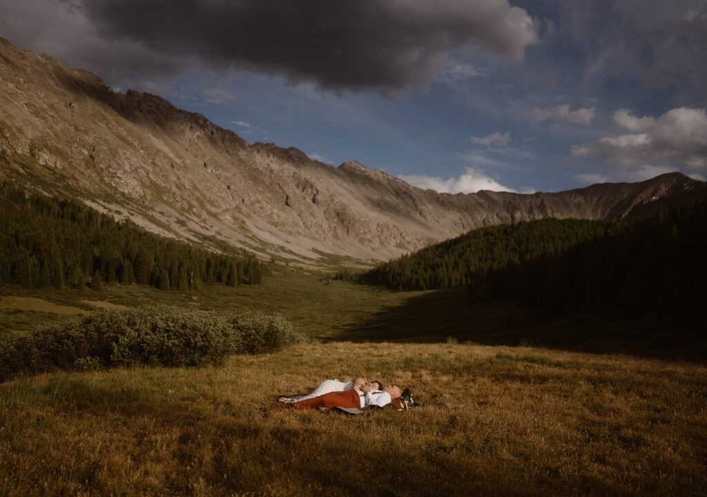 Bride and groom laying in a meadow with mountains in the distance