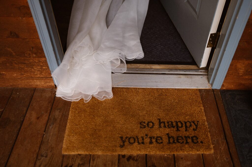 Bride walking through a doorway with a doormat that says "so happy you're here"