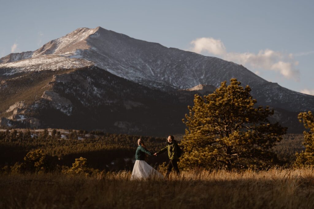 Couple walking through a meadow with snowy mountains in the background on their elopement day