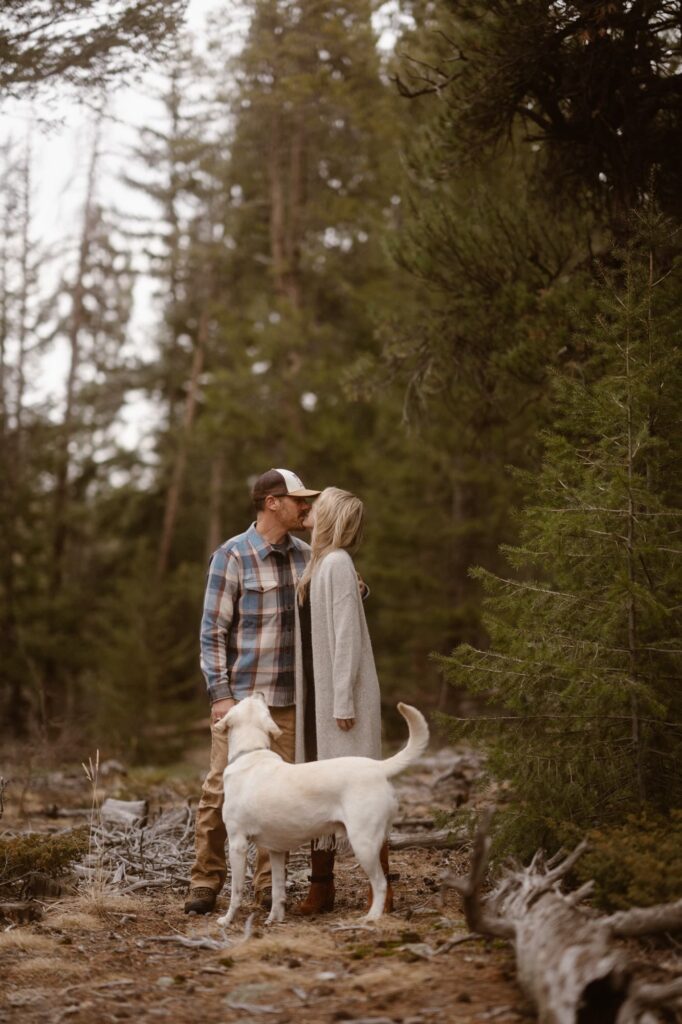 Couple kissing in the forest while their dog looks up at them