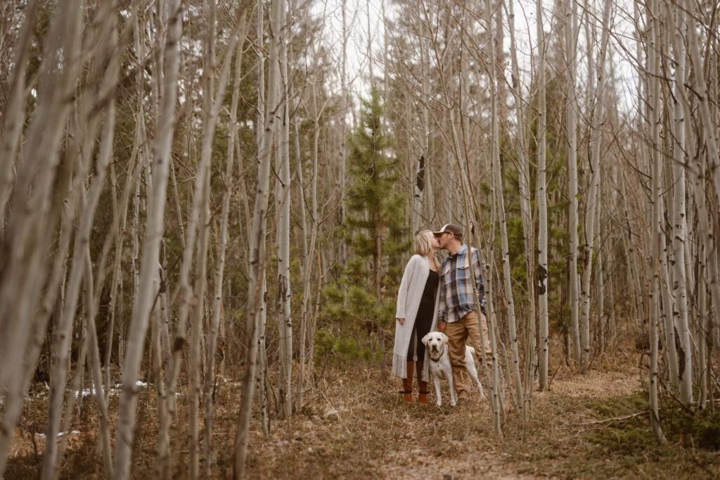Couple kissing in the aspen grove while their dog looks at the camera
