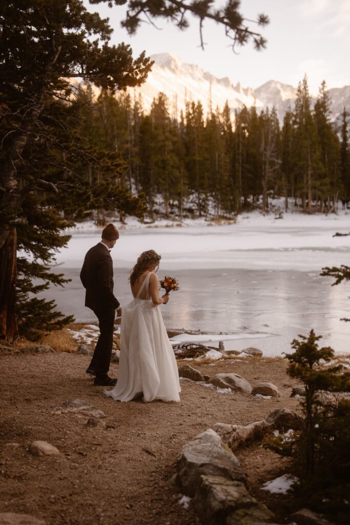 Bride and groom stopping to admire a frozen lake in Rocky Mountain National Park on their wedding day