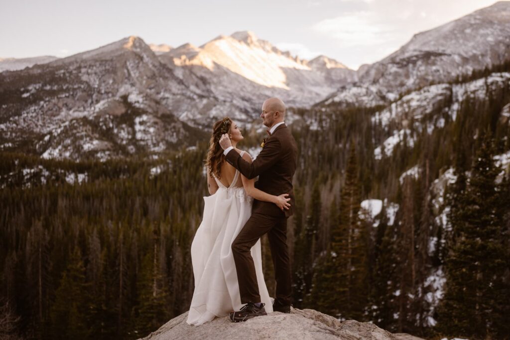 Groom tucking hair behind his wife's ear with snowy mountains in the distance