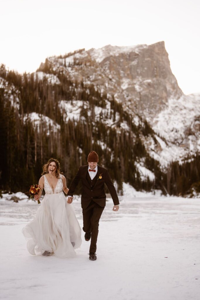 Couple running on frozen Dream Lake on their elopement day