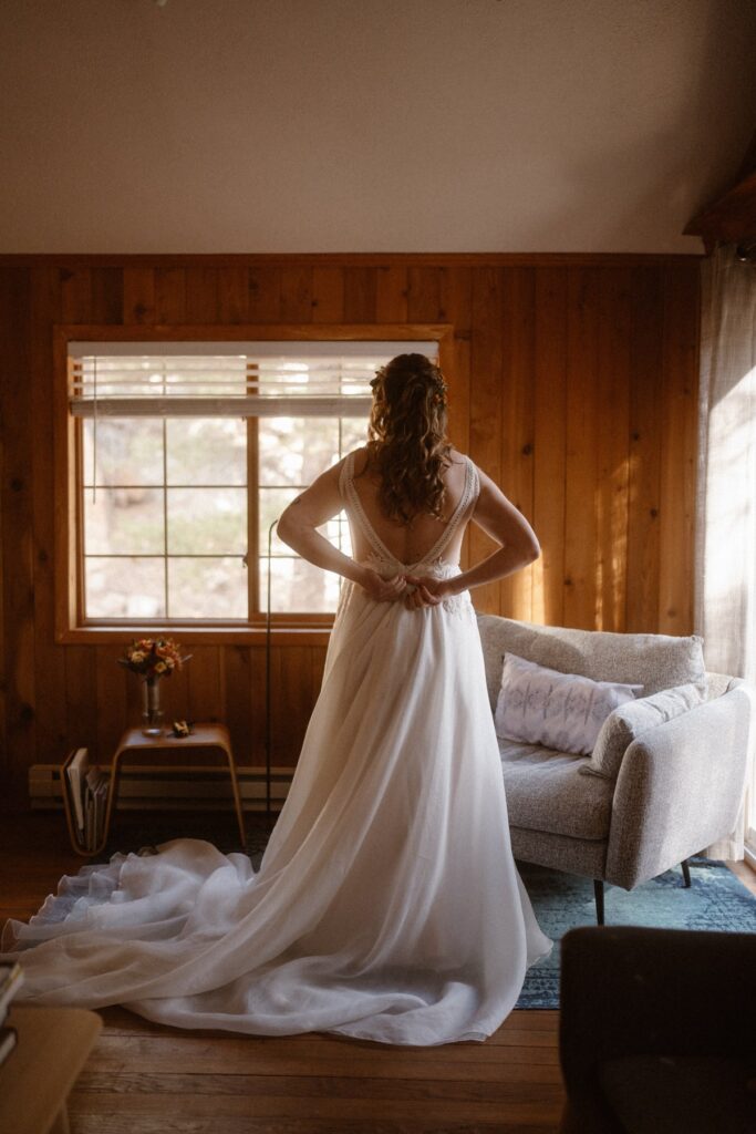 Bride zipping up her wedding dress in a quaint cabin