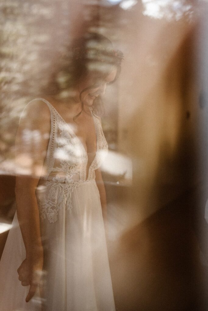View of bride getting ready for her elopement day through a window in a cabin