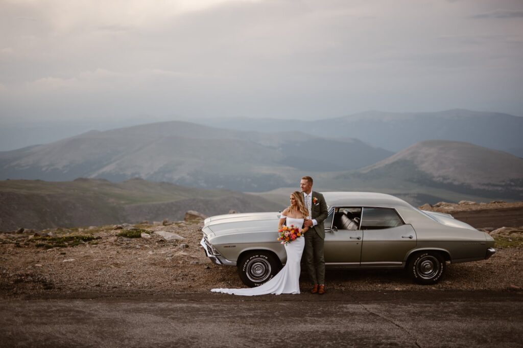 Bride and groom with vintage car on a  mountain top