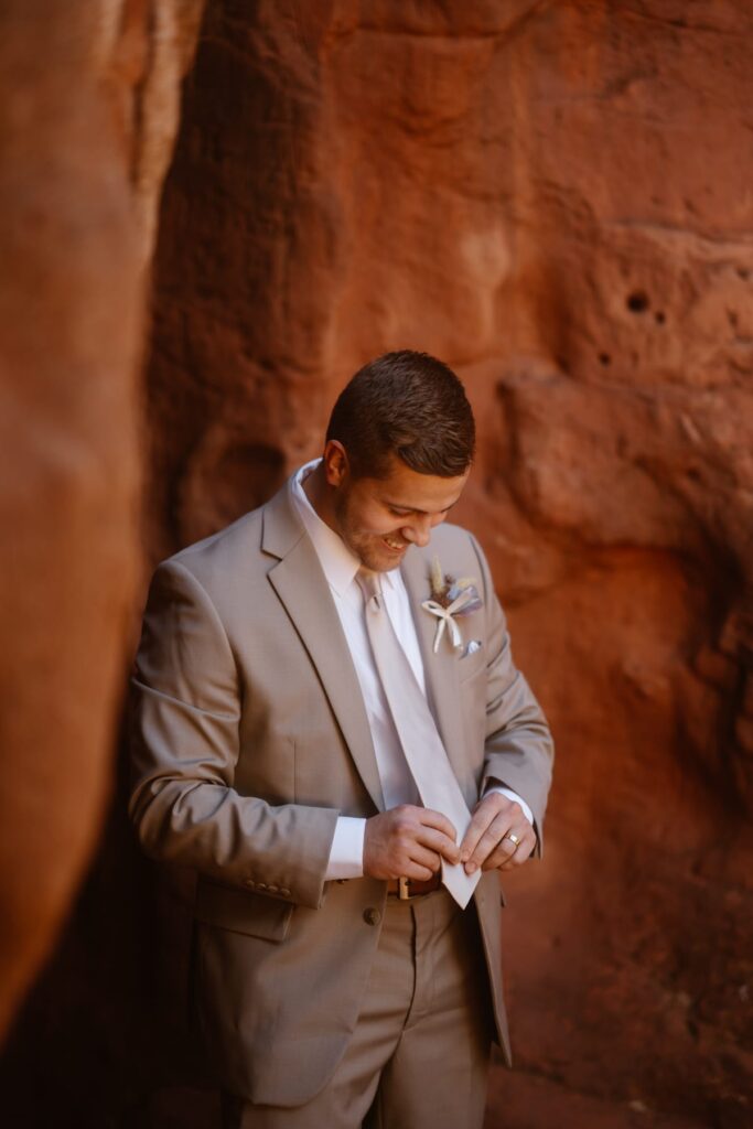 Groom adjusting his tie on his Coloradowedding day with red rocks in the background