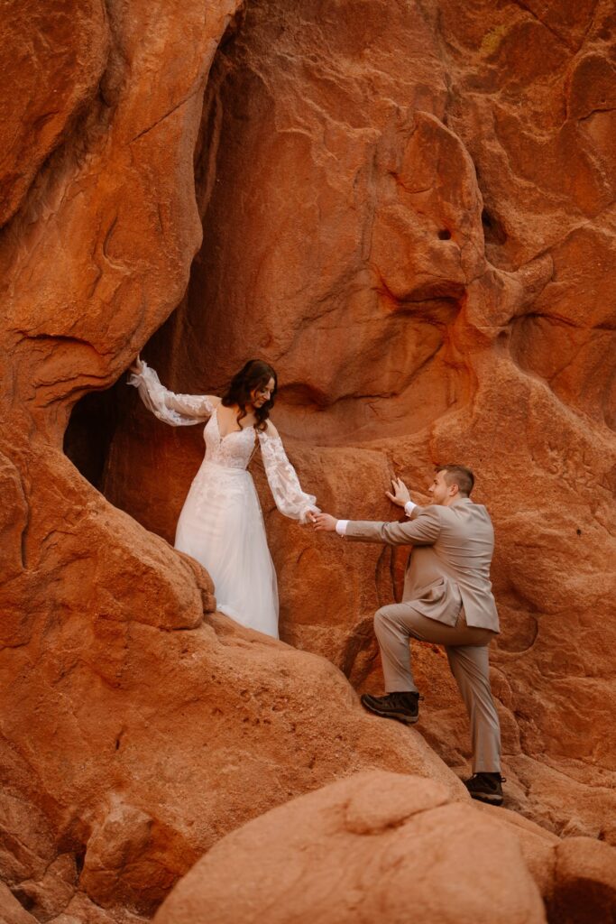 Bride climbing up a rock wall in Colorado and reaching for her groom