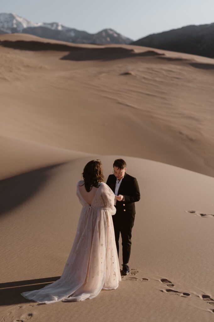 Couple exchanging vows high on the sand dunes in Colorado with mountains in the background