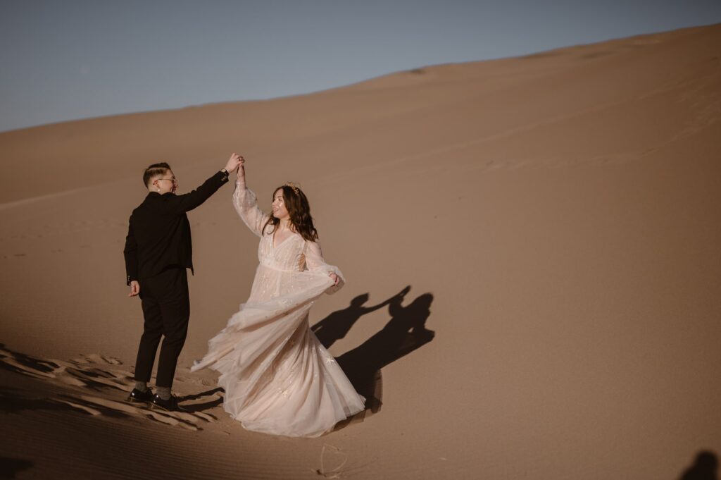 Couple spinning and dancing on sand dunes during their elopement
