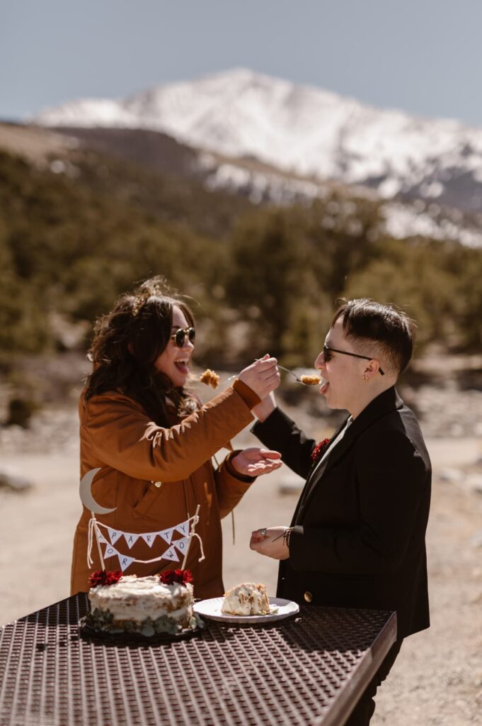 Couple sharing first bites of wedding cake in the mountains