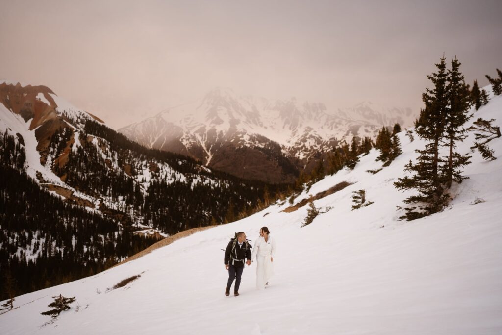 Wedding couple hiking up a snowy mountain as the sun comes up