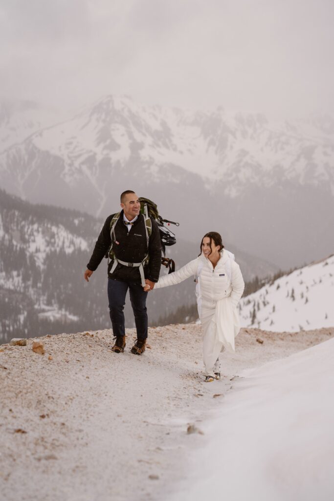 Couple holding hands and hiking up a mountain on their wedding day in Ouray