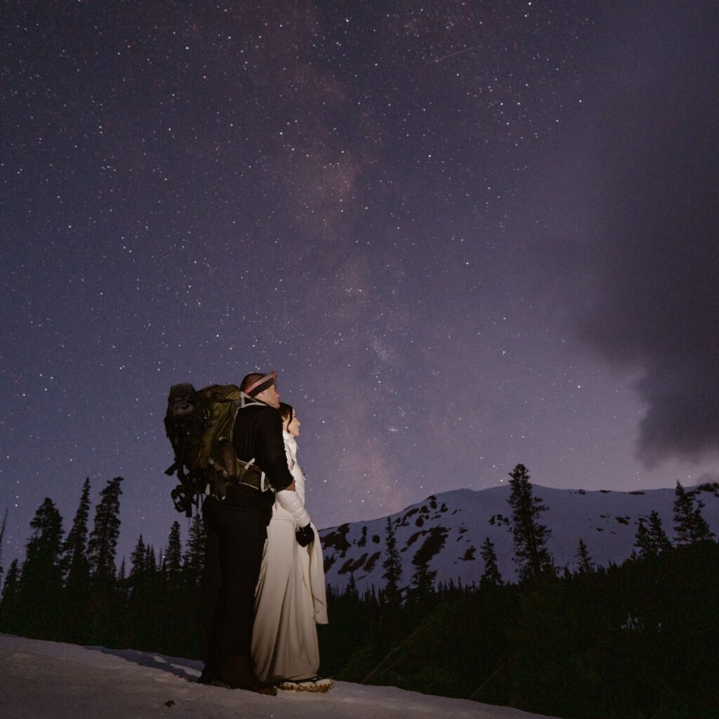 Bride and groom hiking under a starry night sky in the mountains